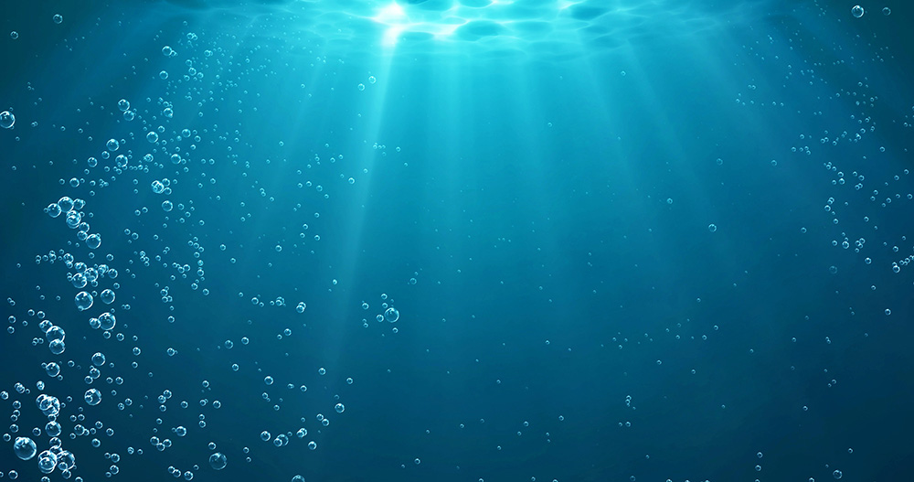 Imagem do fundo do mar, em tons de azul, com bolhas de água e raios de luz descendo da superfície.