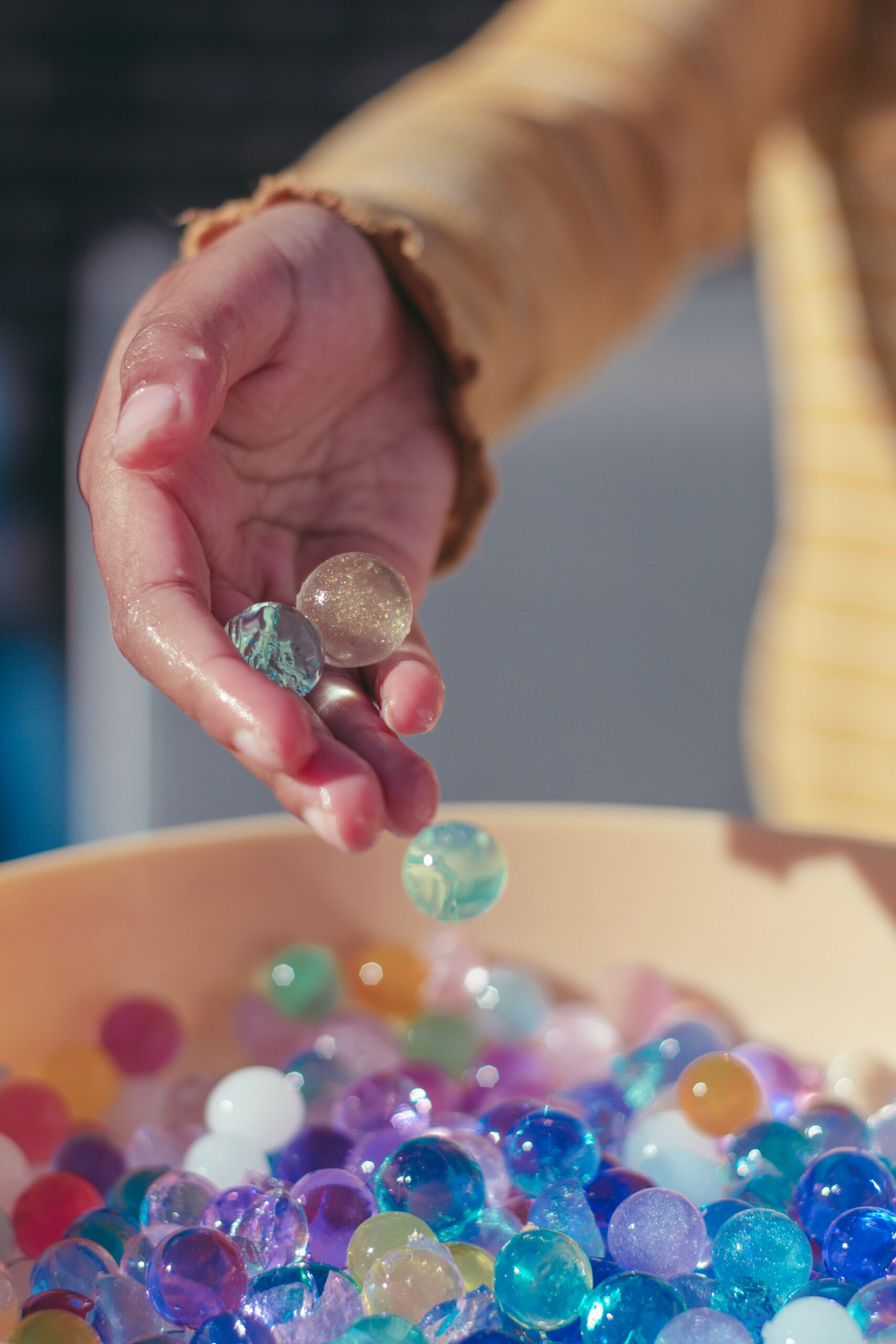 Sinestesia, a associação entre diferentes sentidos no cérebro. Na imagem, uma mão humana de cor de pele branca despejas bolas de gude coloridas em um recipiente de madeira. Créditos: Mieke Campbell on Unsplash